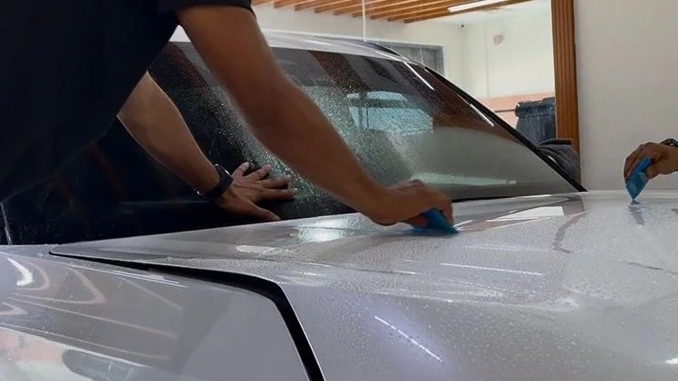 Two fitters working the wet film across the bonnet