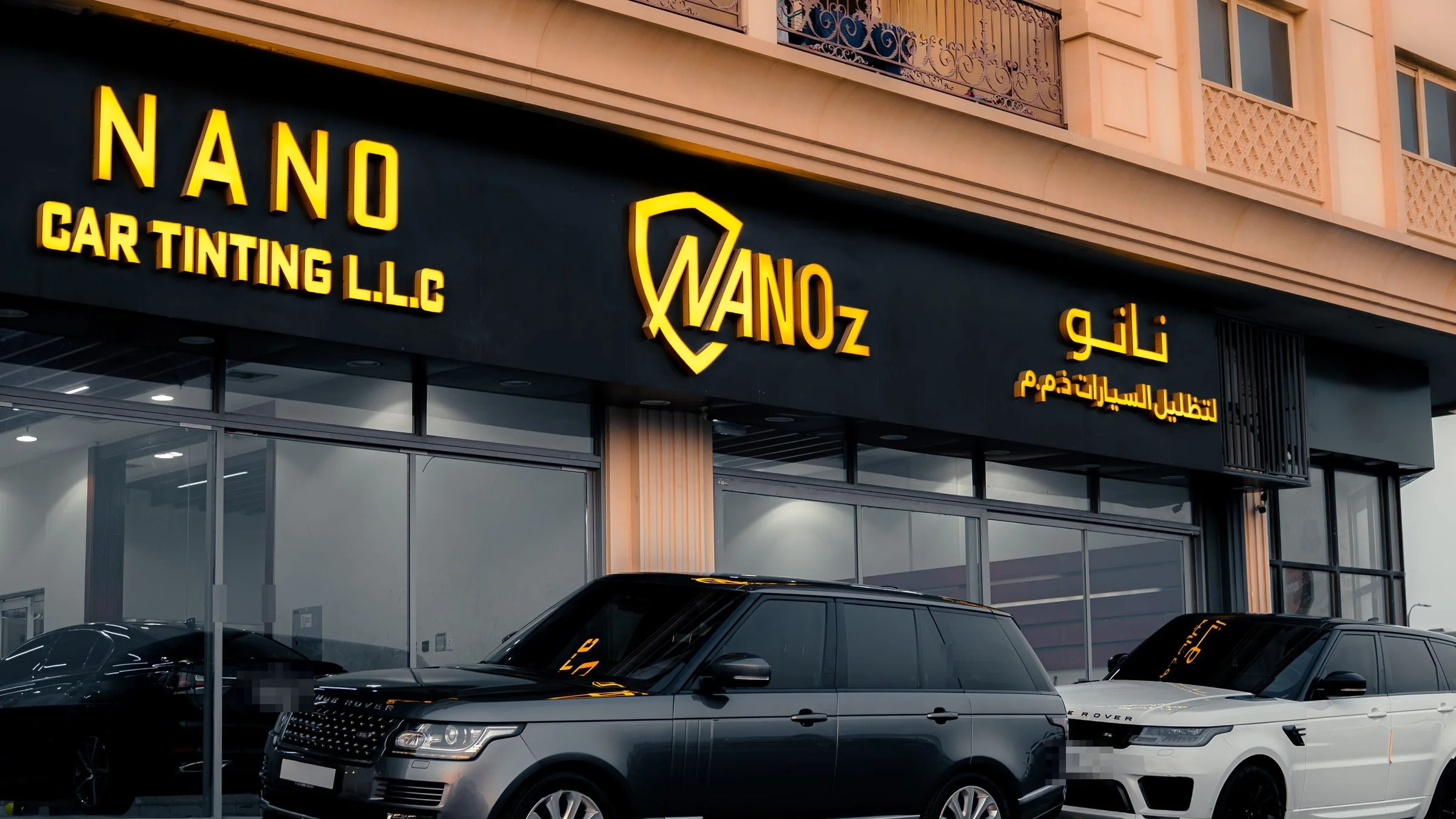 واجهة ورشة الشارقة المضاءة عند الغروب، وأمامها سيارتا رينج روفر