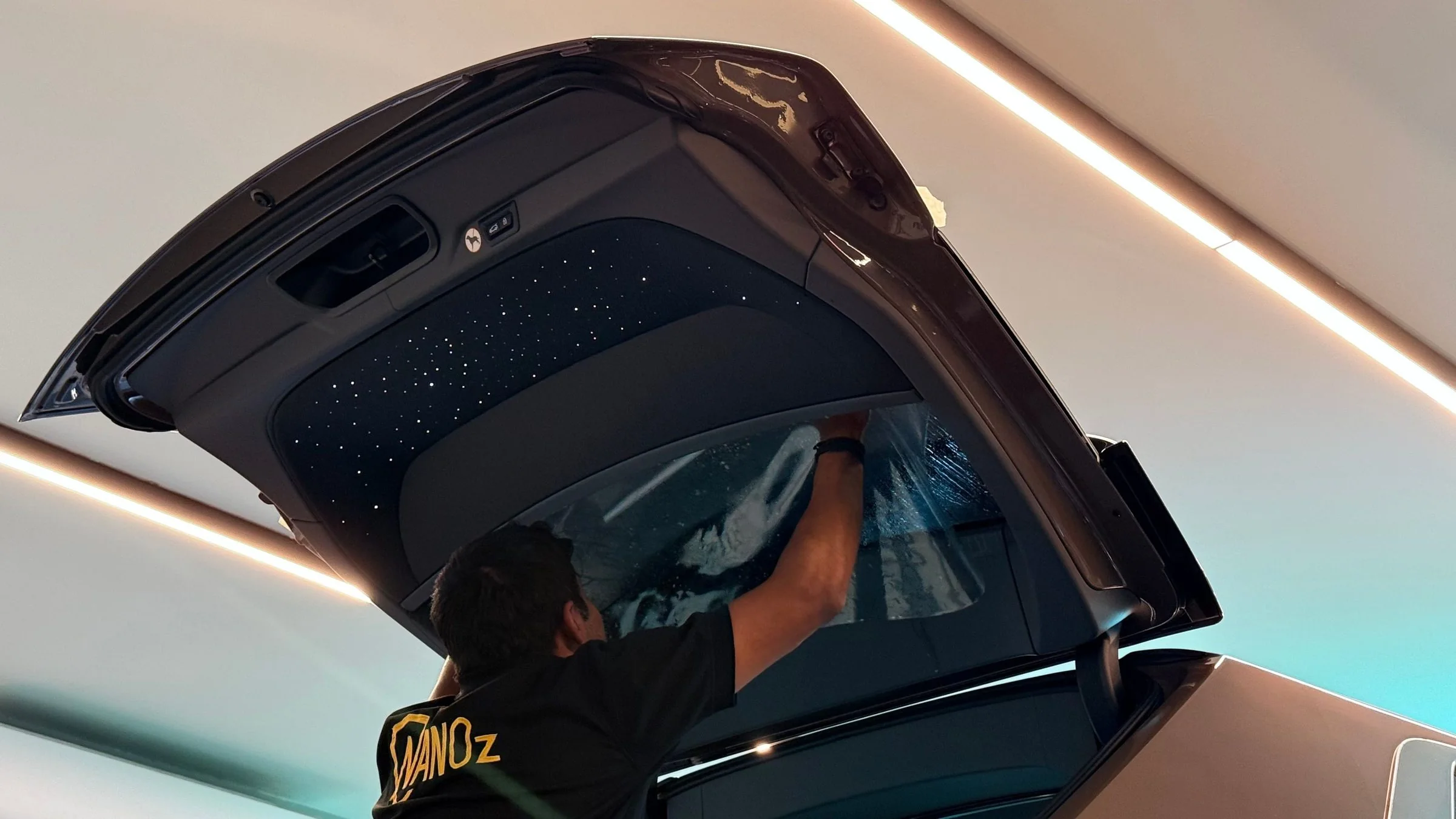 A technician working film across raised tailgate glass under a lit starlight headliner